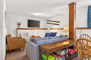 En stue med sofa, stole, et træbord, et fjernsyn og ski på væggen.