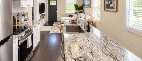 A modern kitchen with a marble countertop, stainless steel appliances, and pendant lighting.