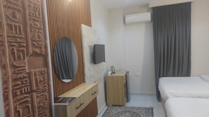 Quarto de hotel com cama, um armário de madeira, uma mesinha, espelho, televisão na parede e janela com cortinas.