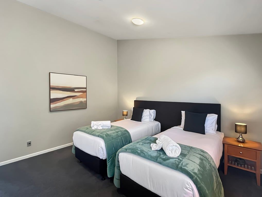 A hotel room with two beds, a painting on the wall, and bedside lamps.