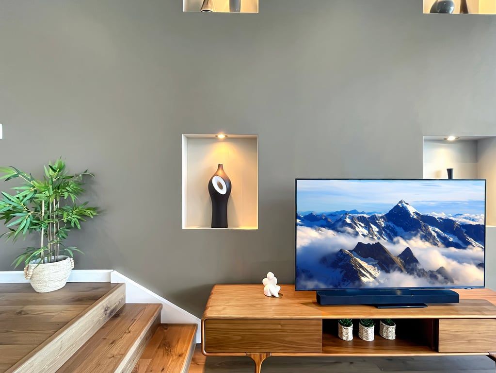 A modern living room with a flat-screen TV on a wooden stand, a potted plant, and a wall-mounted shelf with a decorative item.