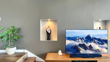 A modern living room with a flat-screen TV on a wooden stand, a potted plant, and a wall-mounted shelf with a decorative item.