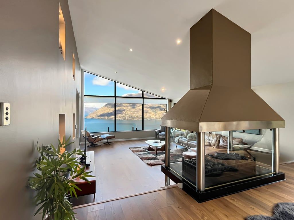 A modern living room with a large fireplace, a view of the sea, and a cozy seating area.