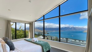 Quarto com uma grande janela que oferece vista para um corpo de água e montanhas.