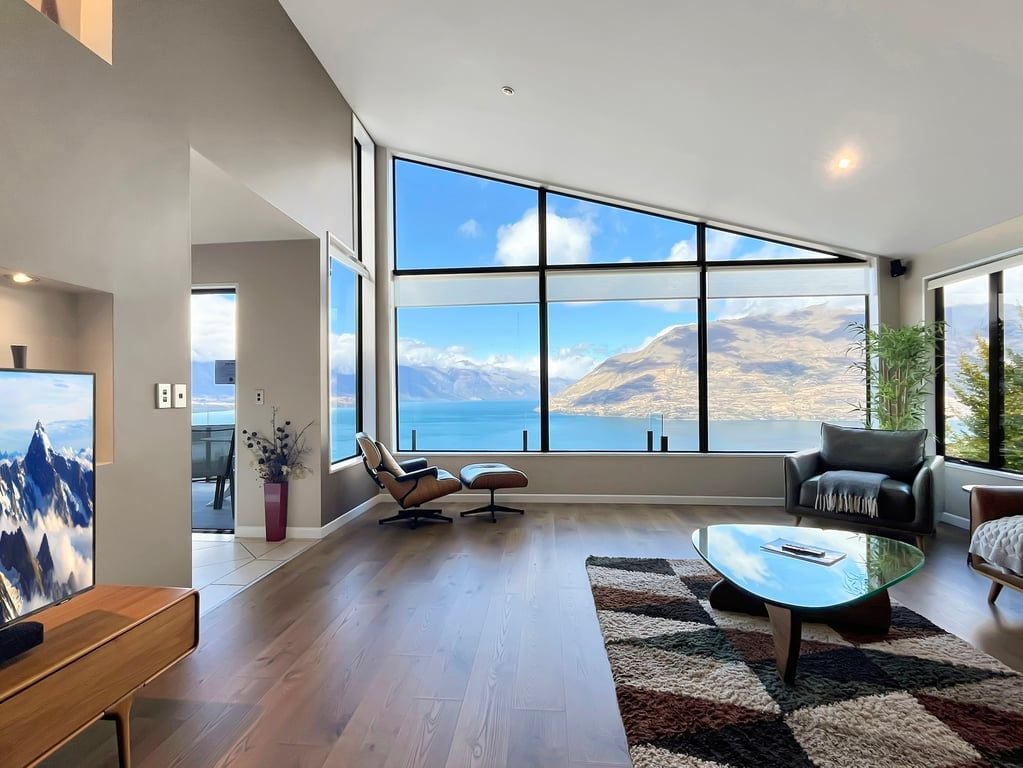 A spacious living room with a large window offering a mountain view, a modern sofa, a glass coffee table, and a flat-screen TV.