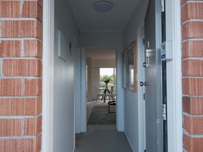 Un pasillo con pared de ladrillo, puertas blancas y vista a una habitación con mesa y sillas.