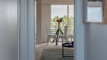 A hallway leading to a balcony with white chairs and a table, a framed picture on the wall, and a view of the cityscape.