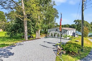 A residential property with a gravel driveway, a flagpole with an American flag, and a house with a visible garage. - Kayaking, fishing, crabbing from private dock, outdoor dining,firepit at sunset. (Topping)