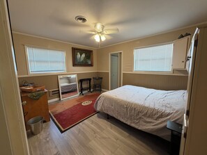Quarto com cama, escrivaninha, cadeira, janela e ventilador de teto.
