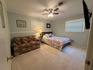 Un dormitorio con cama, sofá, ventilador de techo y ventana con persianas.