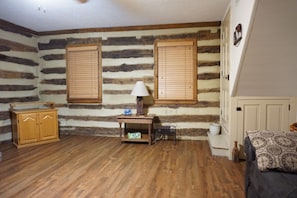 A room with wooden log walls, a wooden cabinet, a small table with a lamp, a bed with patterned bedding, and a white radiator.