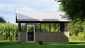 A small, single-story building with a metal roof, a glass door, and a wooden exterior. - Secluded 2-bedroom house with PRIVATE RIVER ACCESS - Petersburg, WV (Petersburg)