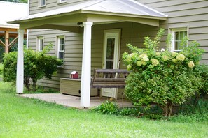 A house with a covered porch, a wooden bench, and a small shed.