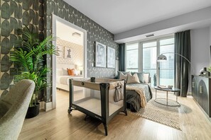 A modern bedroom with a bed, bedside table, lamp, and a view of the city. - Lux Downtown Suite CN Tower Views with Parking | Parking Available (Toronto)
