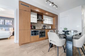 A modern kitchen with wooden cabinets, stainless steel appliances, and a dining area with a glass table and chairs. - Lux Downtown Suite CN Tower Views with Parking | Parking Available (Toronto)