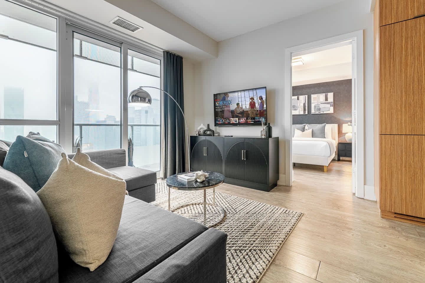 A modern hotel room with a large window, a sofa, a small table, and a TV.