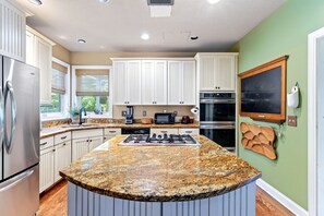 A kitchen with white cabinets, a granite countertop, stainless steel appliances, and a chalkboard wall. - Queen Anne Victorian Home | Mountain Views + Minutes to Downtown Asheville! (Asheville)
