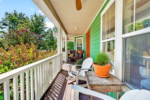 A covered porch with a wooden table and chairs, a potted plant, and a view of a green house. - Queen Anne Victorian Home | Mountain Views + Minutes to Downtown Asheville! (Asheville)