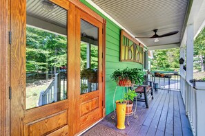 Une véranda en bois, avec une façade peinte en vert, une porte en bois et un ventilateur de plafond.