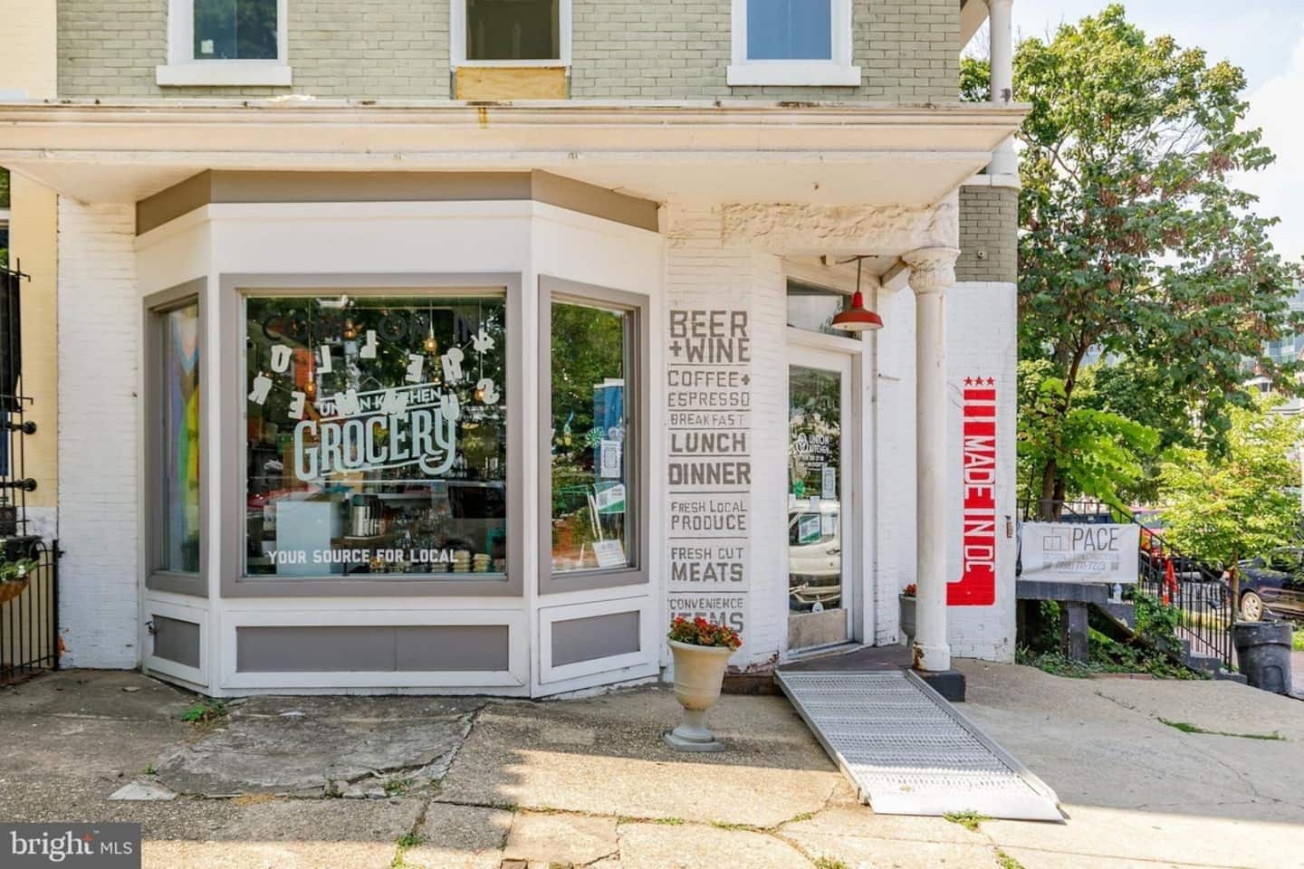A corner store with a signboard listing items like beer, wine, coffee, and local produce.