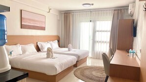 Ett hotellrum med två sängar, ett skrivbord, en stol, en vattenautomat och ett stort fönster med gardiner.
