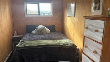 A bedroom with a bed, a dresser, a window, and a framed picture on the wall.