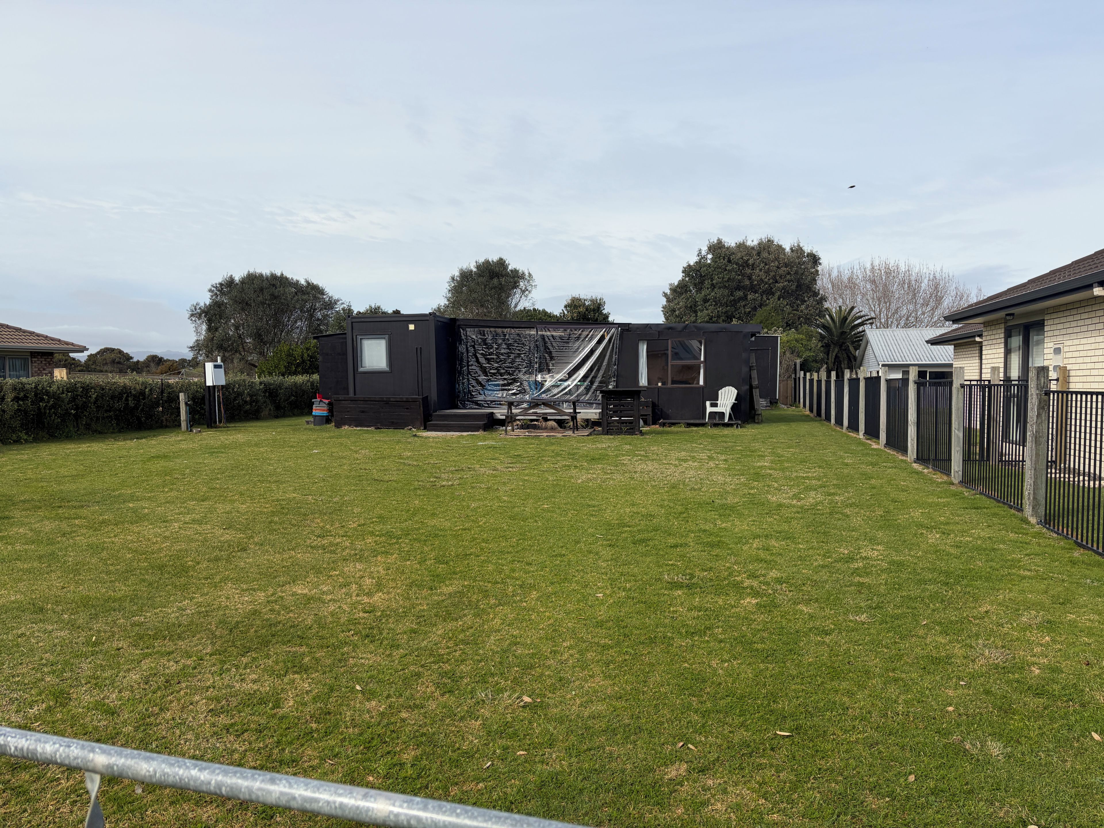 A residential property with a fenced yard, a small outdoor seating area, and a house with a dark exterior.