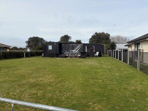 A residential property with a fenced yard, a small outdoor seating area, and a house with a dark exterior.