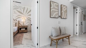 A hotel room with a bed, bedside table, lamp, and a wall with abstract art. - Modern Oceanfront 1BR with Stunning Sea of Cortez Views (Puerto Peñasco)