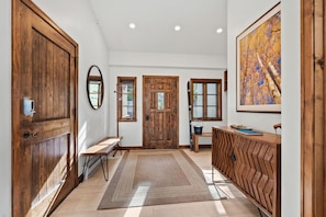 Un couloir avec des portes en bois, un banc, un tapis et un tableau encadré au mur.