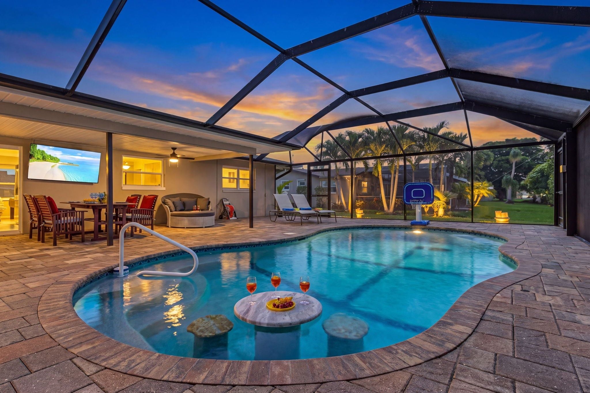 A swimming pool with a sunken hot tub, lounge chairs, and a television screen.