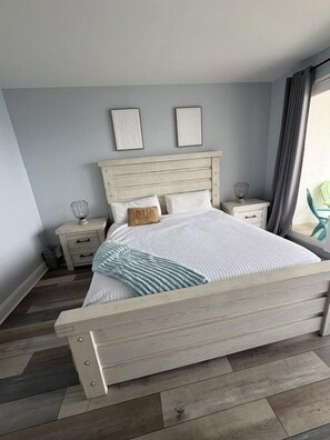 A bedroom with a wooden bed, two bedside tables, a nightstand, and a window with curtains. - Gulf Views-Resort Pools-Steps to the beach! (Panama City)