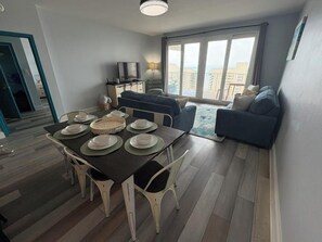 A modern living room with a dining table set for four, a sofa, and a TV. - Gulf Views-Resort Pools-Steps to the beach! (Panama City)