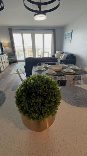 A dining area with a table set for four, a potted plant, and a sofa in the background. - Gulf Views-Resort Pools-Steps to the beach! (Panama City)