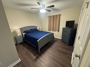 Ein Schlafzimmer mit Bett, Nachttischen, einem Schminktisch und einem Deckenventilator sowie einem Fernseher.