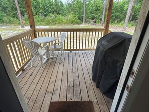 Eine Holzterrasse mit Tisch, Stühlen, einem Grill und Blick auf ein bewaldetes Gebiet.
