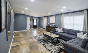 Un salón amplio con un sofá gris, una mesa de centro y una alfombra estampada.
