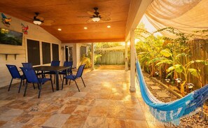 Eine Terrasse im Freien mit Tisch, Stühlen und einer Hängematte, mit Blick auf einen Garten.
