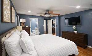Ein Schlafzimmer mit Bett, Deckenventilator, Fernseher und Kommode.