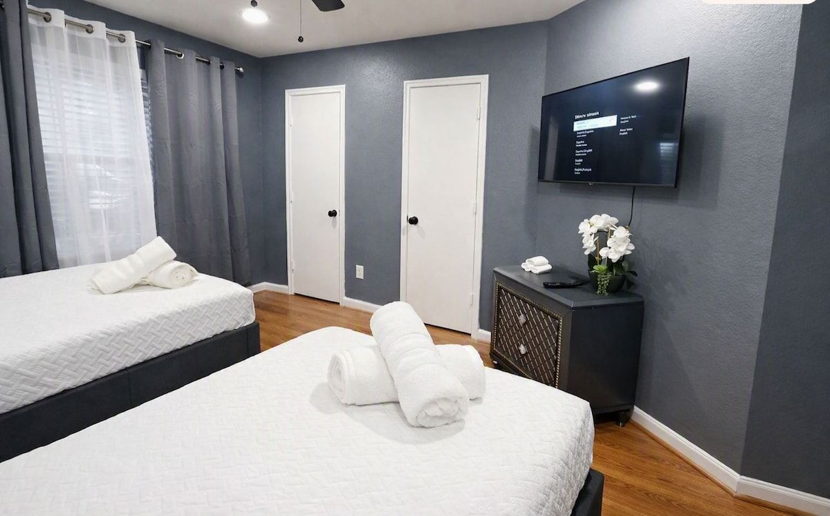 Een hotelkamer met twee bedden, een televisie, een klein tafeltje met een bloemenvaas en een tv aan de muur.