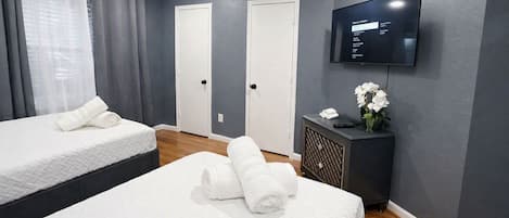 A hotel room with two beds, a TV, a small table with a vase of flowers, and a wall-mounted TV.