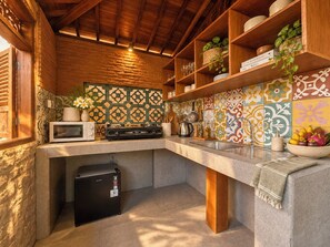 A kitchen with a stone wall, wooden ceiling, and colorful tile backsplash. - Traditional Joglo Pool Villa, Ubud (Ubud)