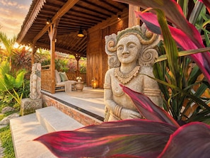 A stone statue, a wooden bench, and a table with a lantern in a covered outdoor area. - Traditional Joglo Pool Villa, Ubud (Ubud)