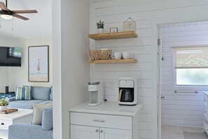 Una cocina moderna con cafetera, estantes de madera y un televisor en la sala de estar.
