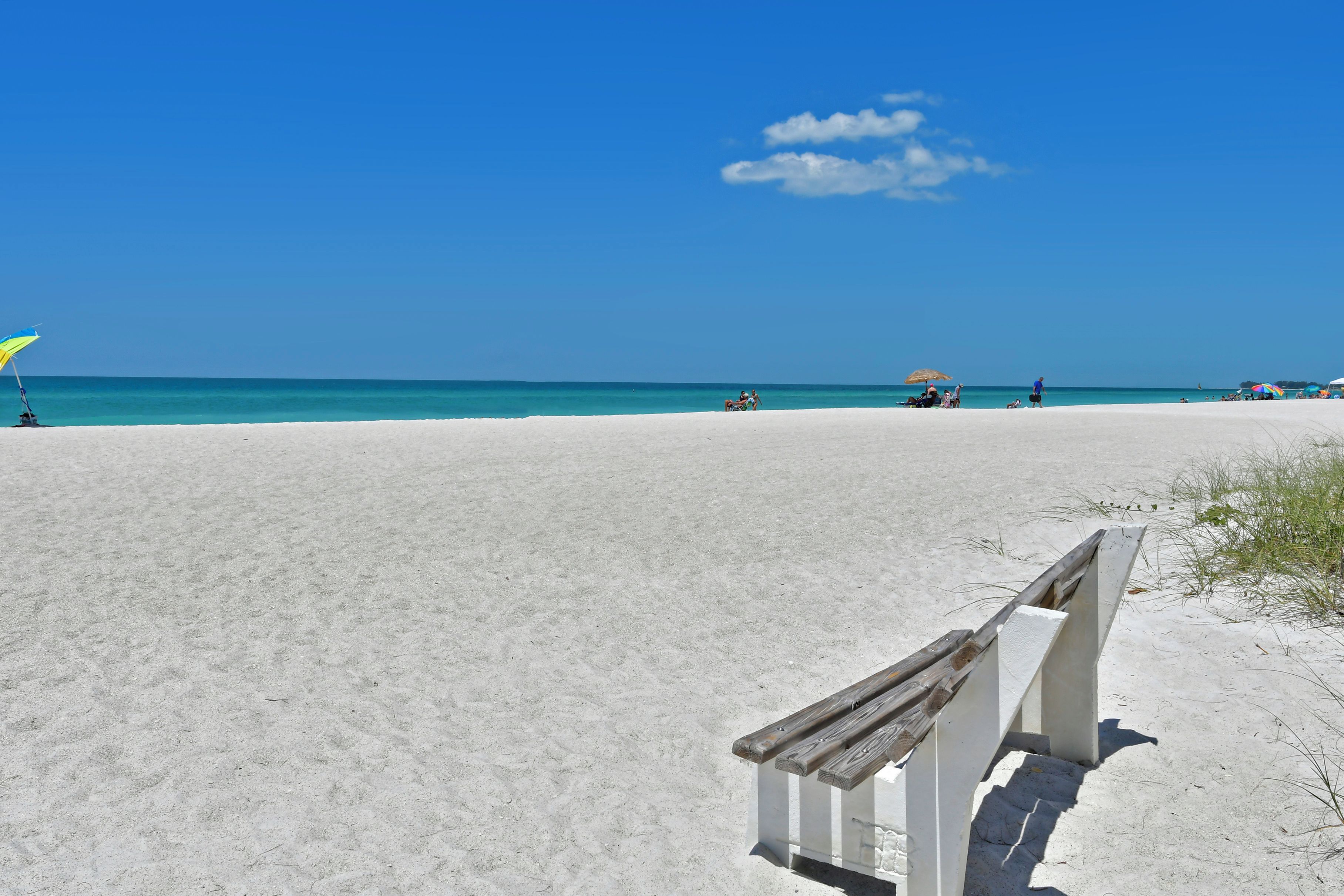 A beach with a wooden bench and a clear blue sky.