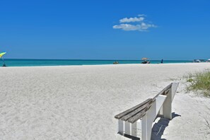 Una playa con un banco de madera y un cielo azul despejado.