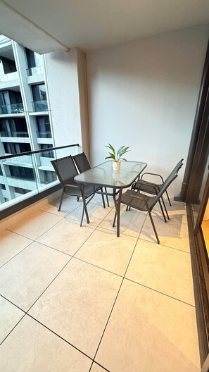 Ein Balkon mit Glastisch und -stühlen, einem Blumentopf und Blick auf ein Gebäude mit Balkonen.