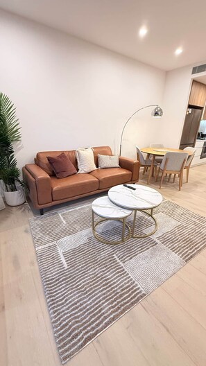 Ein modernes Wohnzimmer mit einer Ledersofa, einem runden Couchtisch und einem Essbereich mit Tisch und Stühlen.