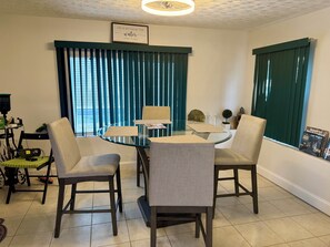 A dining area with a glass table surrounded by four chairs, a small side table, and a wall-mounted picture frame. - 3 BR waterfront house 25 minutes from TAMPA!! Feat. Pool Kayaks, FIshing & Dock! (Ruskin)