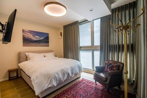 Habitació d'hotel amb un llit gran, una cadira, un televisor fixat a la paret i una finestra amb cortines.